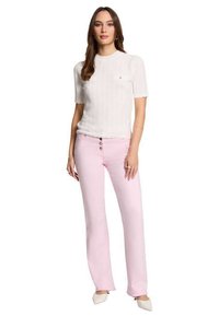 Top bianco a maglia testurizzata con maniche corte, abbinato a pantaloni rosa chiaro a campana con tre bottoni frontali e dettagli in bianco sulle scarpe con la punta.