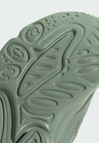Rubber sneaker sole in muted green, featuring textured patterns, grooves, and circular accents for grip and traction.