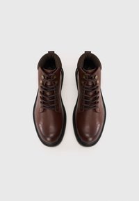 Bottines en cuir marron à bout rond, semelle en caoutchouc noire, œillets en métal et lacets marron. Doublure intérieure douce visible par le dessus.