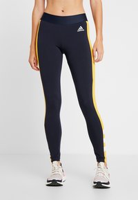 Navy niebieskie legginsy sportowe z żółtymi paskami po bokach i białymi akcentami. Zaprojektowane z wysokim stanem dla wygody i elastyczności podczas aktywności.