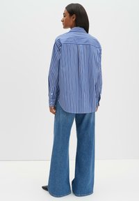 Blau-weiß gestreiftes Langarmhemd mit klassischem Kragen, kombiniert mit hoch taillierten Jeans mit weitem Bein. Glatte Textur und lockere Passform.