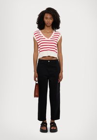 Top de punto blanco recortado con rayas rojas, escote en V, sin mangas; pantalones anchos negros; sandalias negras gruesas; bolso pequeño marrón.