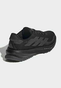 Sort sportssko med tekstureret mesh-overdel, solid gummisål og tre fremtrædende striber på siden. Har en polstret hæl for støtte.