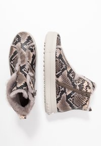 Kotníkové boty se zvířecím potiskem, které mají texturovaný falešný hadí vzor v béžových a šedých tónech, s měkkou podšívkou z falešné kožešiny a bočním zipem.