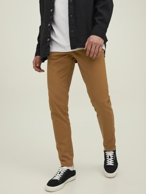 Pantalones ajustados color beige con textura suave; combinados con una camisa de botones negra y zapatillas negras con suelas y cordones blancos.