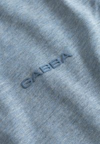 Tessuto blu morbido con il logo "GABBA" in rilievo stampato in lettere blu tono su tono sulla superficie.