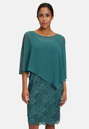 Tüllkleid in Türkis mit transparenter Überlage, Rundhalsausschnitt und seitlichen Schlitzen, schichtweise über einem Spitzenrock mit floralem Muster.