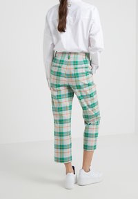 Spodnie w kratę w zielonym, niebieskim, pomarańczowym i białym kolorze, charakteryzujące się wysokim stanem, skróconymi nogawkami i tylnymi kieszeniami. W połączeniu z białymi trampkami.