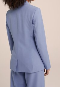 Jasnoniebieska dopasowana marynarka o gładkiej teksturze, z pojedynczym rozcięciem i usztywnionymi ramionami, w połączeniu z dopasowanymi spodniami.