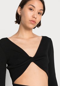 Top cropped de manga longa preto com canelado, com decote em V profundo e detalhe torcido na frente, apresentando uma abertura na cintura e textura suave.