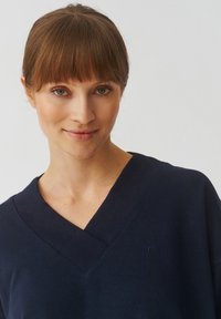Navyblauwe V-hals sweater van zacht materiaal, met een subtiel geborduurd logo aan de linkerkant en geribbelde halslijn en manchetten.