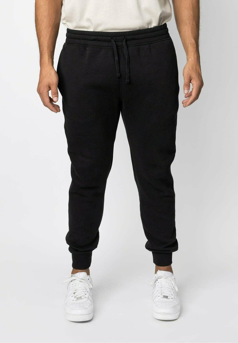 Svarta bomullsjoggers med resårmidja och ankle cuffs. Har en dragsko och sidofickor. Bärs tillsammans med vita sneakers.