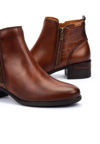 Bruna läderankelboots med en glänsande finish, som har en sidodragkedja och krokodilpr präglade accenter. Låg klack med staplad design, elegant form.