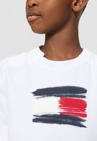 Weißes Baumwoll-T-Shirt mit einem mutigen Pinselstrichdesign in Marineblau, Rot und Weiß. Rundhalsausschnitt mit lockerer Passform.