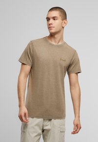 Brun kortærmet bomulds t-shirt med rund hals. Har diskret broderet tekst på brystet. Blød tekstur og afslappet pasform.