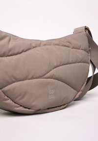 Borsa crossbody imbottita in beige tenue con una fantasia trapuntata. Presenta un logo bianco e una tracolla regolabile per il massimo comfort.