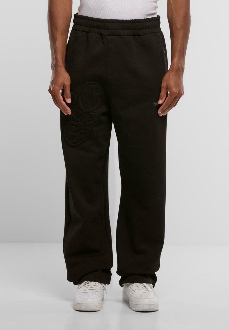 Sorte sweatpants lavet af blødt stof, udstyret med elastisk talje og prægede logo detaljer på venstre ben. Stylet med hvide sneakers.