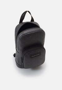 Black leather backpack with textured logo pattern, featuring a front zip pocket and top handle. Rounded shape and smooth finish.