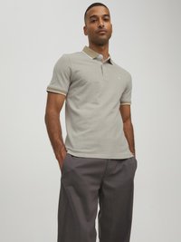 Hellgraues Poloshirt mit geripptem Kragen und braunen Akzenten, mit kurzen Ärmeln und schmaler Passform. Kombiniert mit dunkelgrauen Hosen.