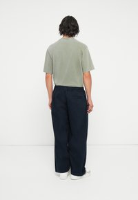 Zaļš kokvilnas T-krekls un tumši zilas brīvas bikses. T-kreklam ir klasiska apaļa kakla izgriezums; biksēm ir elastīga josta un sānu kabatas.