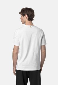 T-shirt bianca in cotone con colletto rotondo e maniche corte. Presenta un piccolo dettaglio nero, giallo e rosso sul retro del collo.