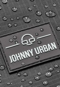 Fekete textúrájú anyagon vízcseppek láthatók, egy téglalap alakú logóval, amelyen fehér betűkkel szerepel a "JOHNNY URBAN" felirat.
