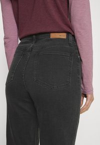 Černé džínové kalhoty s vysokým pasem, s dvěma zadními kapsami a koženou nášivkou na pasu. Nošeny s vrstveným růžovým topem.