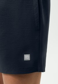 Shorts de bain bleu marine en tissu texturé, avec poche latérale et une étiquette grise portant l'inscription "SWIM WEAR by mey." L'ourlet est droit avec des détails subtils.