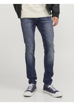 Jeans de denim azul con un corte Slim Fit, que presentan un sutil lavado, y combinados con zapatillas navy con cordones y suelas blancas.