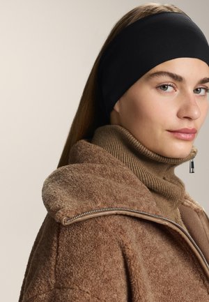 Černý látkový pásek na hlavu, který se nosí s béžovým pleteným rolákem a hnědou fleecovou bundou s detaily stříbrného zipu.