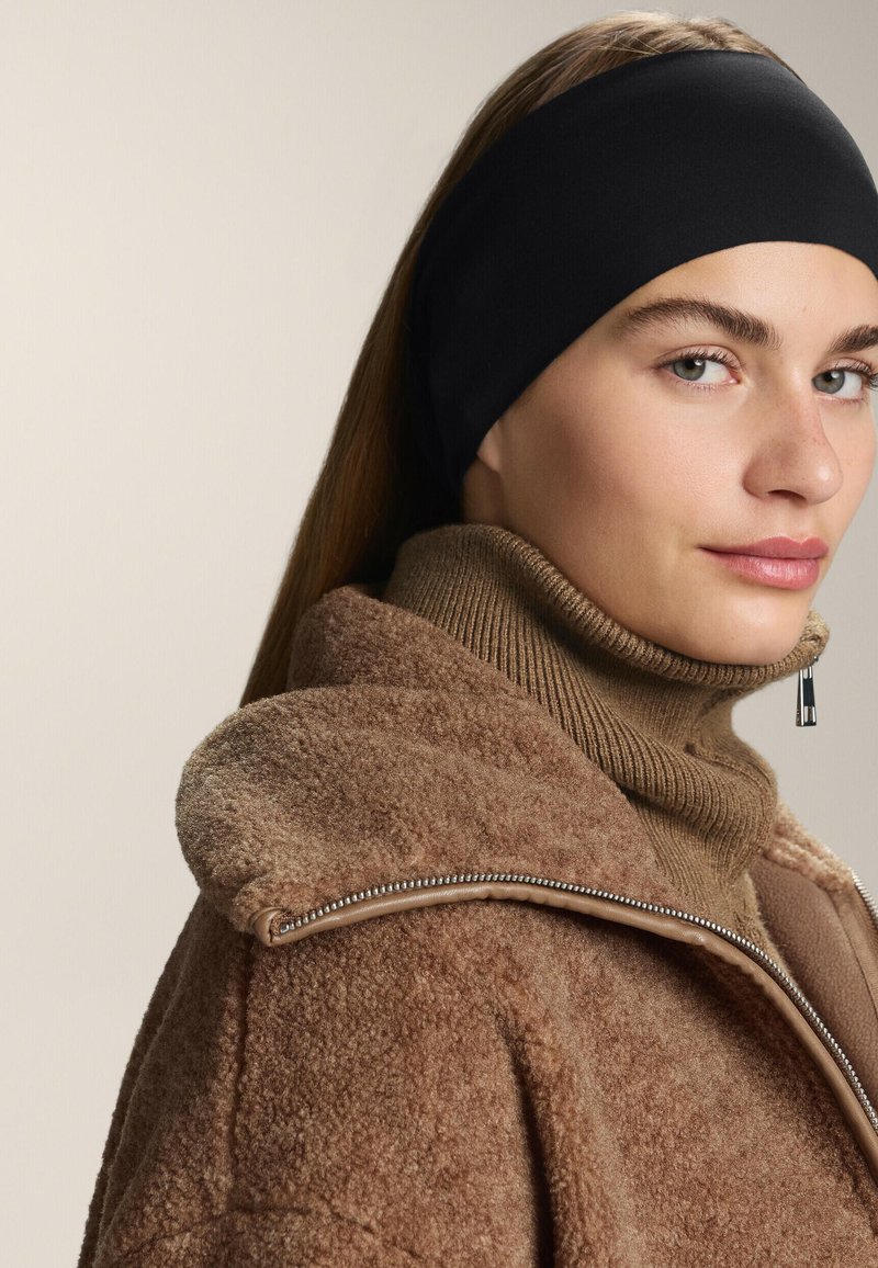 Černý látkový pásek na hlavu, který se nosí s béžovým pleteným rolákem a hnědou fleecovou bundou s detaily stříbrného zipu.