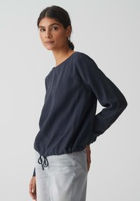 Blusa a maniche lunghe di colore blu navy, realizzata in tessuto morbido, con scollatura arrotondata, orlo elastico e dettaglio con cordoncino in vita.