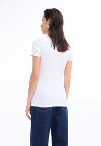 Top blanco de manga corta con un diseño ajustado, textura de canalé y un escote redondo, combinado con jeans azul oscuro.