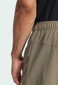 Olivengrønne shorts med en tekstureret overflade, der har elastisk talje og sidelommer. Hånd placeret på siden for støtte eller greb.