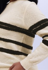 Pull tricoté présentant une base crème avec des rayures texturées vert foncé, un col rond et des manches ajustées. Matière douce et chaude avec des poignets côtelés.