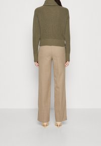 Pull encolure roulée côtelé vert olive associé à un pantalon large beige et des chaussures à talons nude, vu de dos.