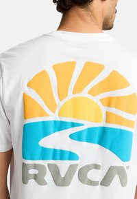 Witte katoenen t-shirt met een grote grafische afbeelding van een gele zon en een blauwe rivier, met de tekst "RVCA" in het grijs op de achterkant.