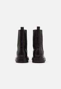 Bottines en cuir noir avec une texture lisse, des panneaux élastiques sur les côtés et des languettes pour un enfilage facile. Semelles en caoutchouc légèrement surélevées.