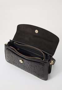 Fekete bőr kézitáska, domborított márkájú logóval, aranyszínű fémszerelvényekkel és cipzáras belső zsebbel. Suéd béléssel ellátott fedél, patentos záródással.