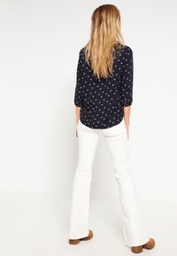 Blusa navy con piccolo motivo floreale bianco, maniche a tre quarti, abbinata a pantaloni bianchi a campana e stivali con tacco marroni.