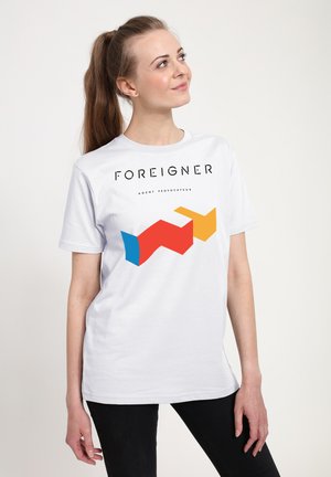 T-shirt en coton blanc avec un graphique audacieux en rouge, bleu, jaune et noir portant le texte "FOREIGNER AGENT PROVOCATEUR" à l'avant.