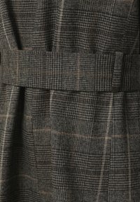 Tessuto a quadri grigio scuro e marrone con passante e cintura coordinati, caratterizzato da una miscela di motivi a quadri piccoli e grandi.