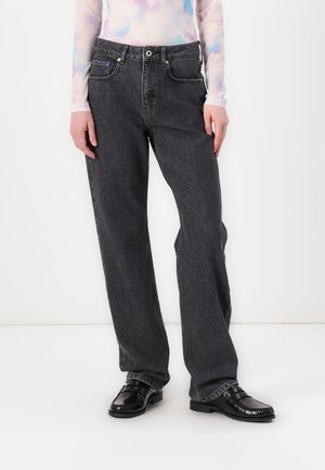Zwarte, wijde jeans met een vervaagde textuur, voorzien van vijf zakken, riemlussen en contrasterende stiksels. Gecombineerd met glanzende zwarte loafers.