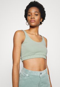 Top cropped verde claro com textura canelada e bainha elástica. Apresenta alças largas e detalhes discretos com o logótipo.