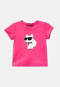 T-shirt en coton rose avec un graphique d'un chat blanc portant des lunettes de soleil noires, des perles dorées et un motif de cravate sur son col.
