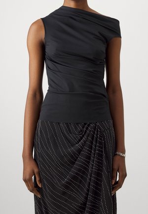 Femme portant un haut noir sans manches et à épaules dénudées ainsi qu’une jupe noire à motifs ondulés blancs en points, debout les bras détendus le long du corps.