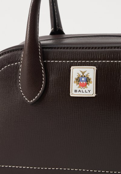 Sac en cuir marron foncé avec des coutures blanches, deux poignées et un patch logo rectangulaire Bally avec un blason et du texte sur le devant.