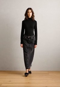 Melnas pieguļošas turtleneck krekls, augstās jostas melna džinsa svārki līdz potītēm, ar jostu, kombinēti ar melnām kurpēm. Vienkāršs fons.