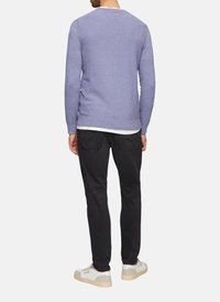 Lichtpaarse gebreide trui met een gestructureerde afwerking, ronde halslijn en een relaxte pasvorm, gedragen over een wit shirt en gecombineerd met zwarte broek.
