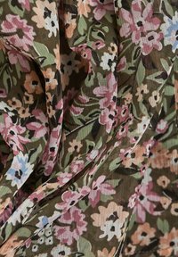 Gros plan sur un tissu avec un motif floral en fleurs roses, blanches et bleues sur un fond vert et marron.